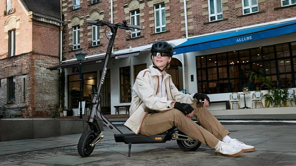 Electric scooter rider sitting beside an electric scooter on a city street.