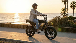 Rider cruising a black NAVEE KG05 moped-style fat tire electric bike along a coastal paved trail at golden hour sunset.